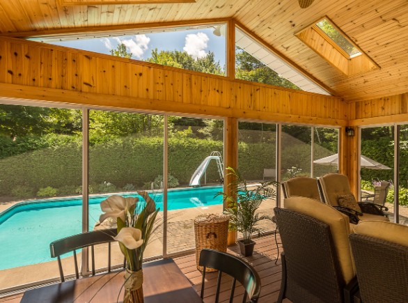 Porche de madera cerrado con acristalamiento lateral junto a una piscina