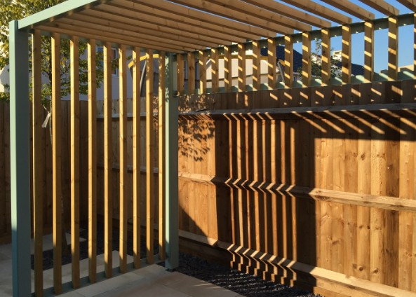 Pérgola de madera con listones verticales adosada a un cerramiento de jardín