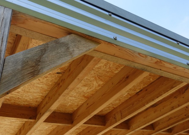 Detalle del alero de un porche con estructura de madera y cubierta metálica